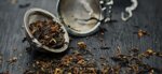 loose leaf tea in tea egg, tea leaves scattered on wooden table