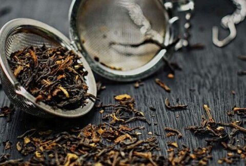 loose leaf tea in tea egg, tea leaves scattered on wooden table